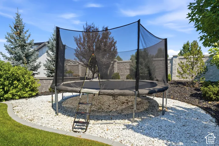 Landscaped backyard featuring white stone ground cover, a manicured lawn, perimeter block wall fencing, and mature evergreen trees
