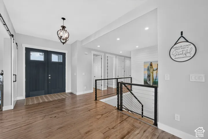 Double entry doors featuring a dark finish, wood-finish flooring, metal railing with horizontal cable infill, and shiplap wall accents