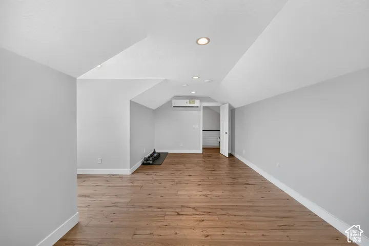 Finished room with wood-finish flooring, vaulted ceilings, recessed lighting, and wall-mounted climate control unit