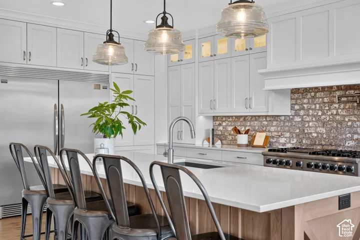 Kitchen featuring white cabinetry with glass-front uppers, a central island with a stone countertop, an exposed brick backsplash, recessed lighting, and industrial-style pendant fixtures