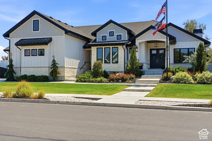 Modern exterior featuring board-and-batten siding, stone masonry accents, a covered front entryway, multi-gabled roofline, and custom black window framing