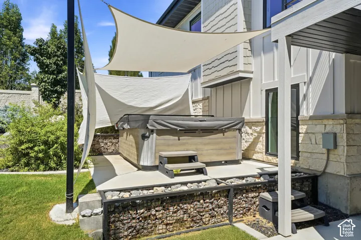 Outdoor living area featuring a built-in hot tub on a concrete patio, stone-accented exterior siding, and a metal-framed retaining wall filled with natural stone