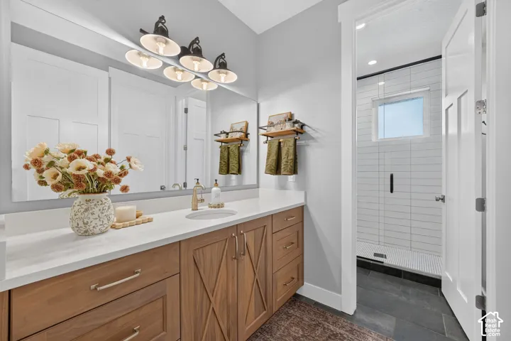 Bathroom vanity with wood-finish cabinetry, white countertop, integrated sink, metal hardware, and multi-light wall fixture