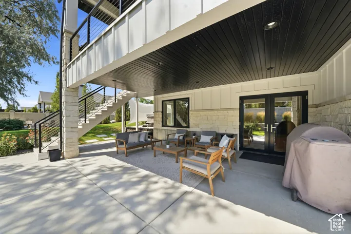 Covered concrete patio featuring board-and-batten siding, natural stone veneer masonry, recessed ceiling lighting, and metal staircase with cable railing