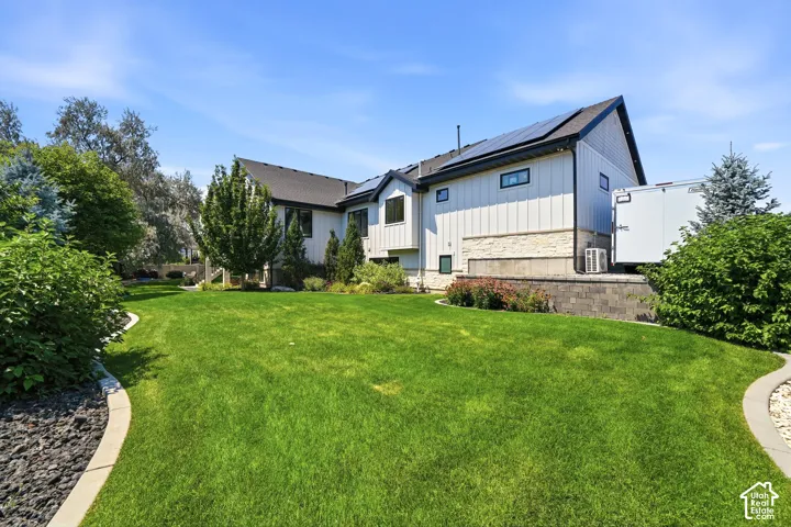 Expansive lawn featuring mature landscaping, stone-veneer exterior accents, vertical siding, and roof-mounted solar panels