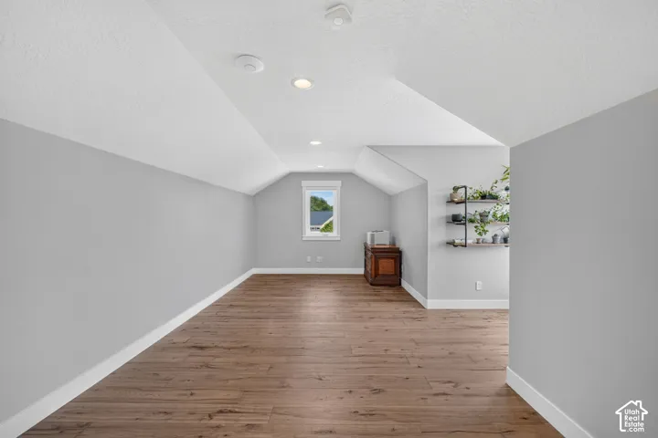 Vaulted ceilings, wood-finish flooring, recessed lighting, and wall-mounted shelving