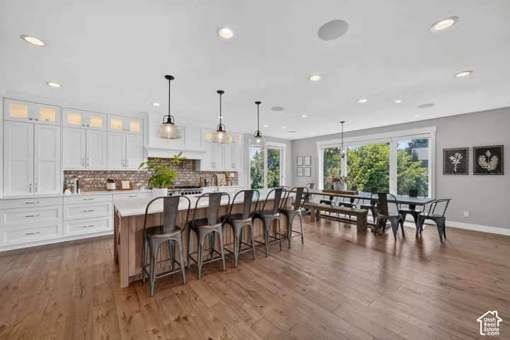 Kitchen featuring white cabinetry, wood-finish flooring, central island with quartz countertop, brick backsplash, and recessed lighting