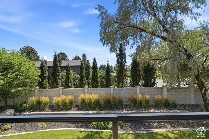 Rear outdoor space featuring a textured concrete masonry wall, manicured lawn, ornamental grasses, and mature evergreen trees