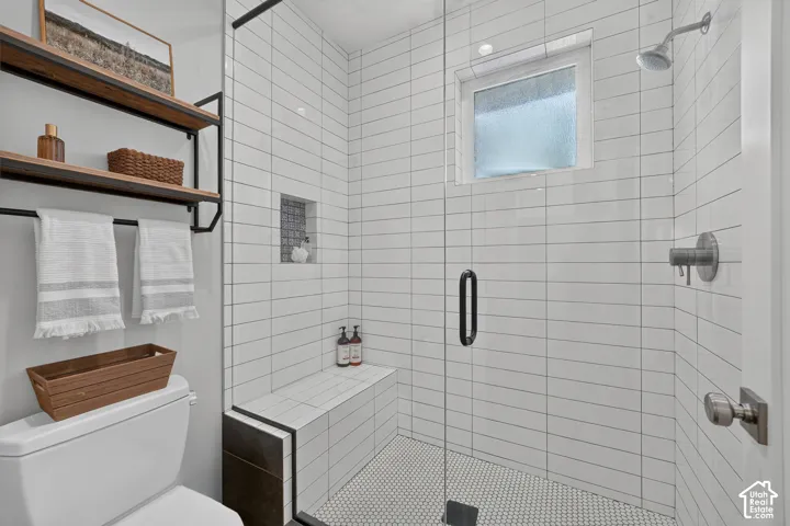 Walk-in shower featuring white subway wall tile, mosaic floor tile, built-in tiled bench, recessed wall niche, and glass enclosure with matte black hardware
