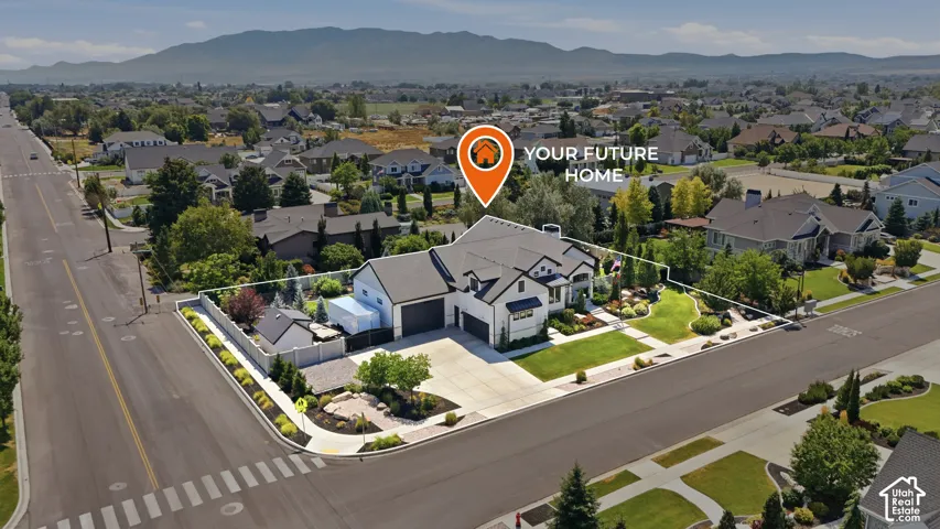 Aerial view of a corner lot property featuring a multi-car garage, concrete driveway, manicured landscaping, and mountain backdrop