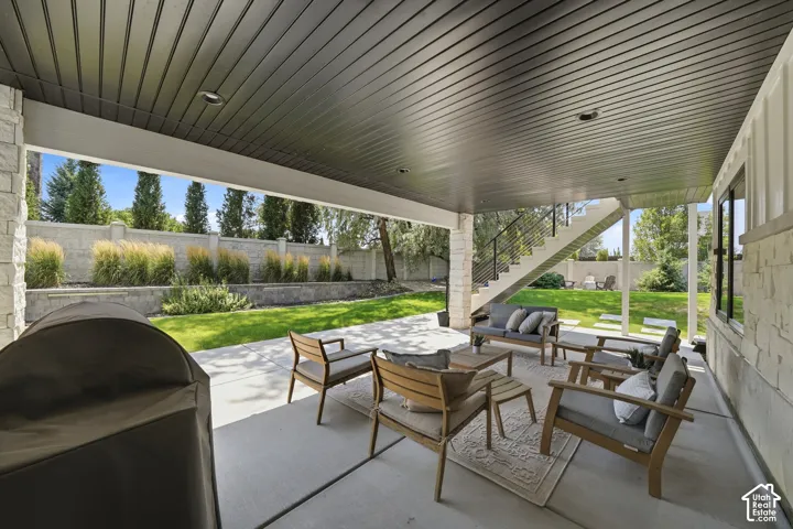 Covered concrete patio featuring recessed lighting, a stone-pillar support, built-in staircase with metal railings, and a terraced backyard with a perimeter wall