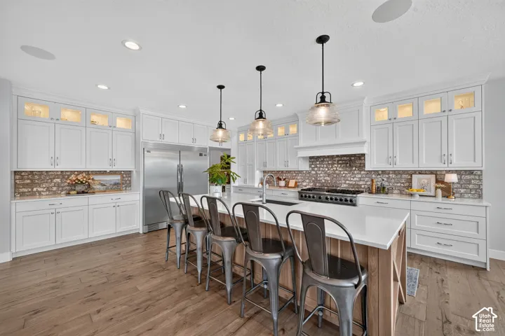 Kitchen featuring shaker-style cabinetry, exposed brick backsplash, oversized quartz-topped island, wood-finish flooring, and industrial-style pendant lighting