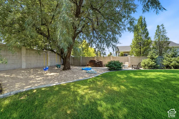 Private backyard featuring a manicured lawn, a defined gravel area, concrete block perimeter fencing, mature trees, and landscaping