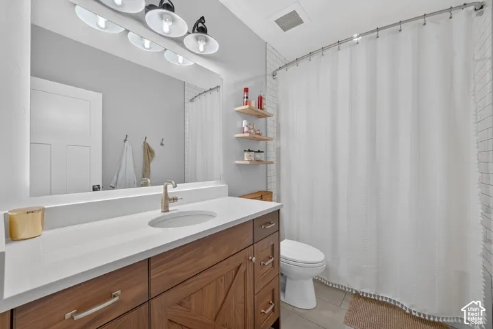 Wood-finish vanity with a stone countertop, undermount sink, multi-light fixture, large wall mirror, and built-in wall shelving