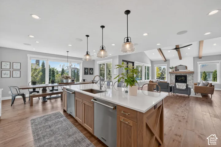 Open-concept kitchen featuring an oversized island with quartz countertops, custom wood-finish cabinetry, stainless steel appliances, pendant lighting, and wide-plank wood-finish flooring