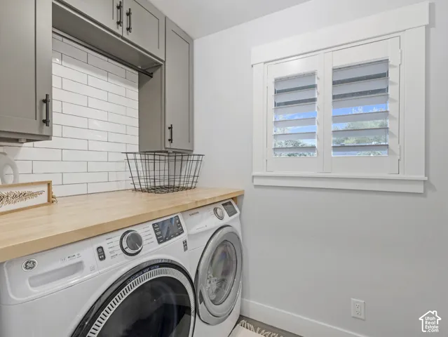 Laundry room featuring custom gray cabinetry, wood-finish countertop, white subway tile backsplash, and window fitted with plantation shutters