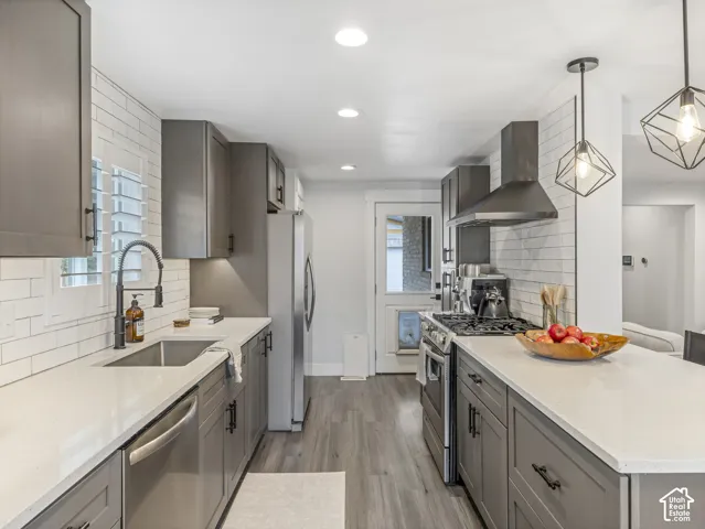 Kitchen featuring gray shaker-style cabinetry, quartz countertops, white subway tile backsplash, stainless steel appliances, and wood-finish flooring