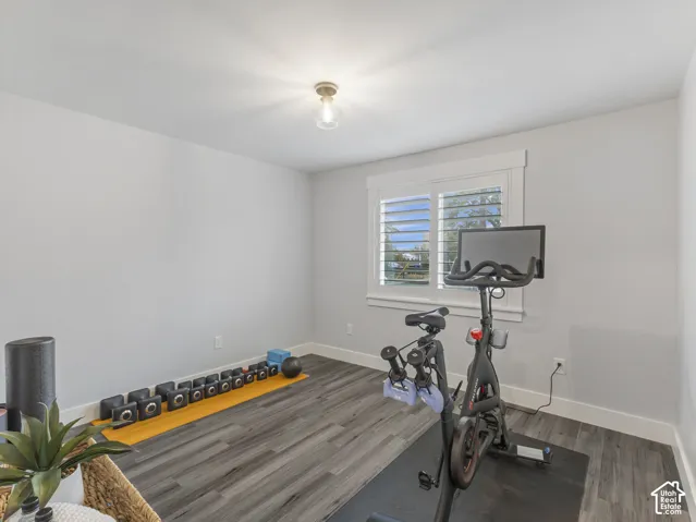Room featuring wood-finish flooring, white walls, and a window equipped with plantation-style shutters