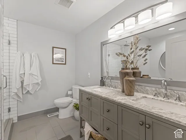 Dual-sink vanity with a stone countertop and framed mirror, undermount sinks with polished chrome faucets, and a glass-enclosed shower with white subway tile
