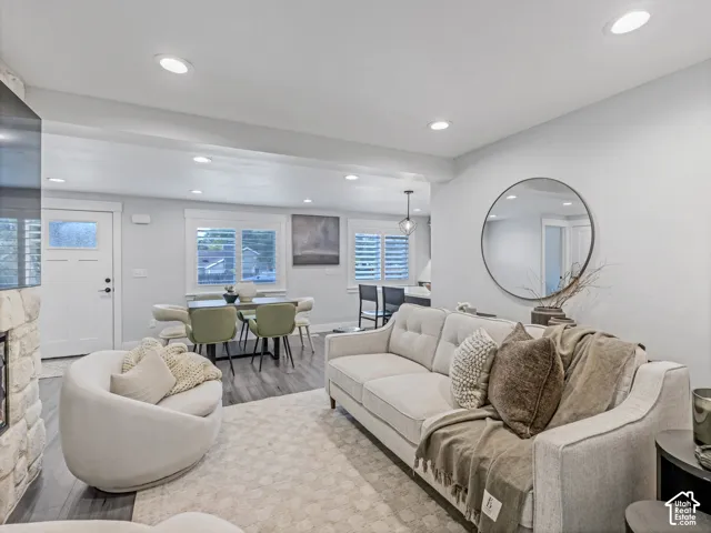 Living area featuring light-toned wood-finish flooring, recessed lighting, white stone-surround fireplace, and white shutters on multi-pane windows