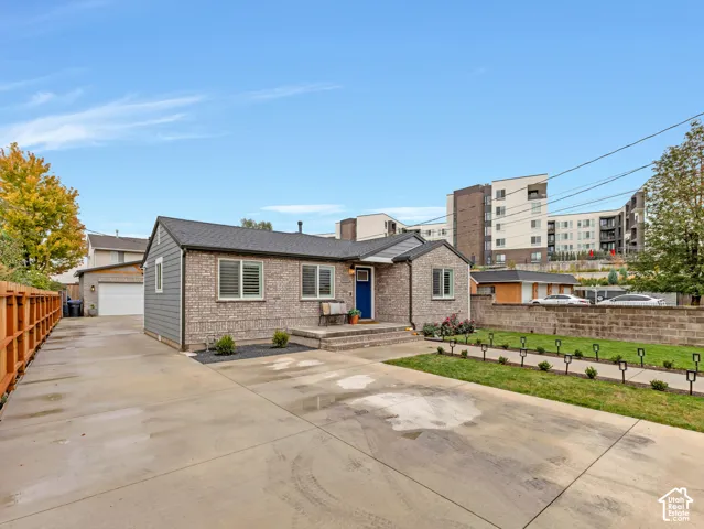 Single-story residence with a brick and lap siding exterior, concrete driveway, detached garage, and a fenced front lawn with a paved walkway