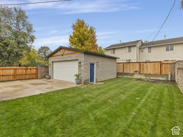 Detached garage featuring textured stone masonry, gable roofline with decorative timber accents, concrete driveway, and enclosed backyard with wood fencing