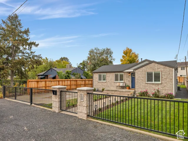 Brick exterior featuring a gated entry, metal perimeter fencing, manicured lawn, and stone-tiled front stoop