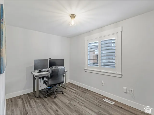 Room featuring wood-finish flooring, white window casing, and interior plantation shutters
