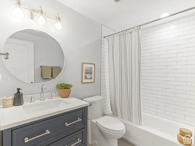Bathroom featuring a dark-toned vanity with a white countertop, circular wall-mounted mirror, three-light polished chrome fixture, and a shower-tub combination with white subway tile surround