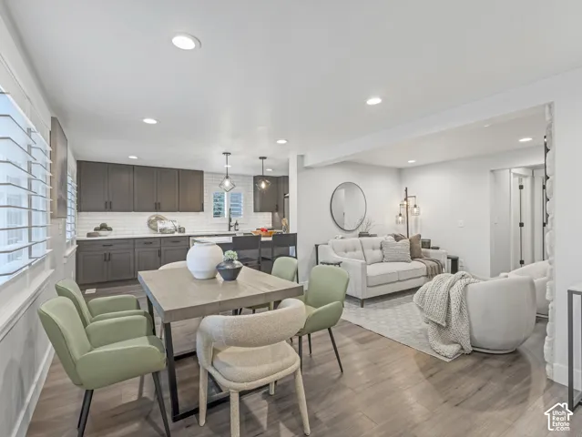 Open-concept living space featuring wood-finish flooring, recessed lighting, white subway tile backsplash, dark-toned cabinetry, and a stone-accented wall finish