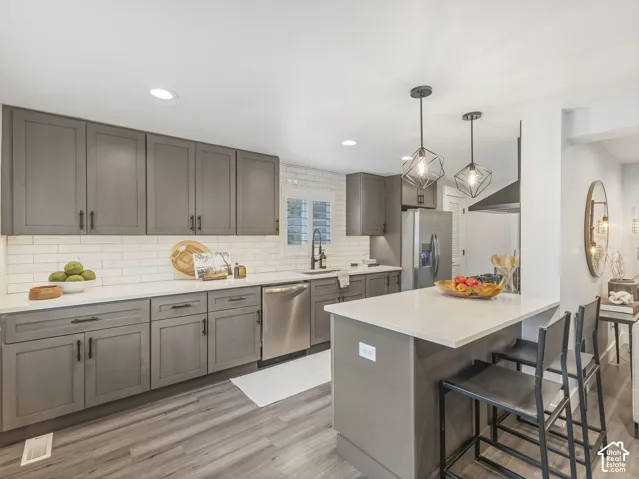 Kitchen featuring grey shaker-style cabinetry, white subway tile backsplash, quartz countertops, wood-finish flooring, and industrial-style geometric pendant lighting