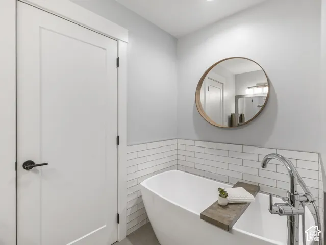 Freestanding soaking tub with chrome floor-mounted faucet, white subway tile wall surround, circular mirror with wood-finish frame, and neutral tile flooring