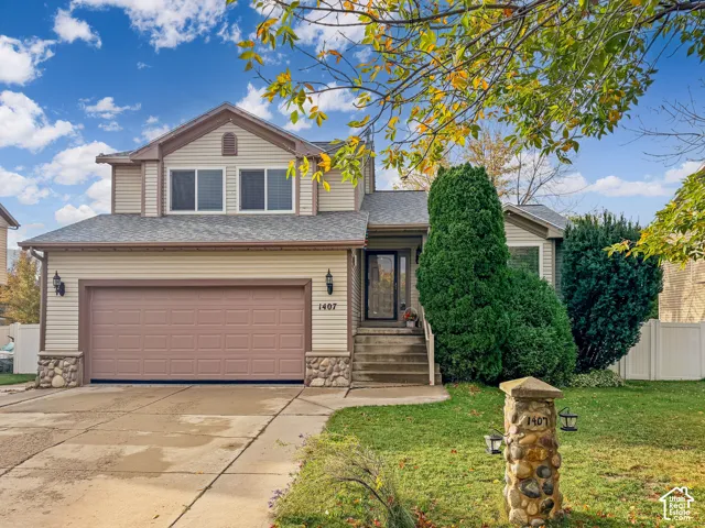Two-story exterior featuring light-toned vinyl siding, river rock stone veneer accents, a dual-car garage, and a covered entryway