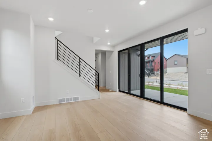 Open-concept interior featuring light LVP flooring, recessed lighting, a horizontal black metal staircase railing, and large multi-panel glass sliding doors