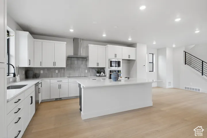 Kitchen featuring white shaker-style cabinetry, a large central island with a solid surface countertop, LVP flooring, a stainless steel chimney-style range hood, and a textured tile backsplash