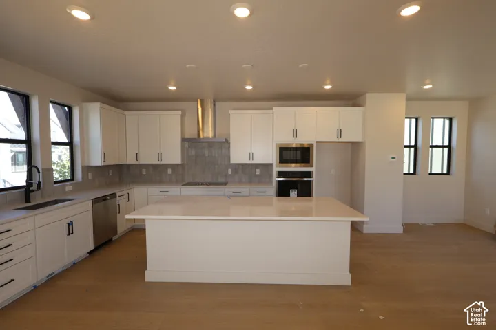 Kitchen featuring white shaker-style cabinetry, quartz countertops, a central island, stainless steel wall-mounted range hood, and recessed lighting
