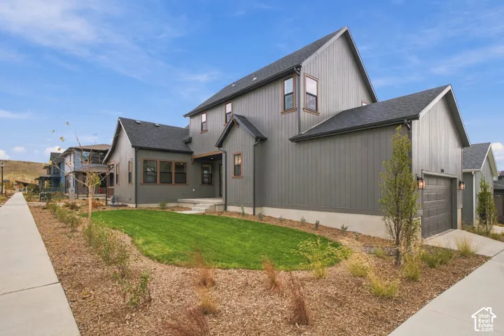 Two-story residence featuring vertical siding, a pitched roofline, an attached garage, and manicured front lawn landscaping