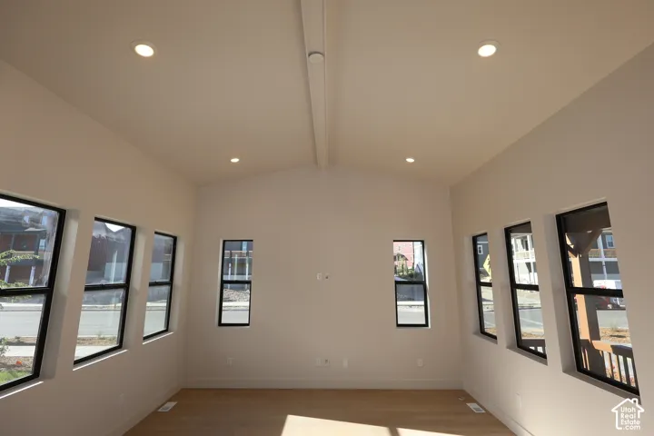Vaulted ceiling with a central ridge beam, recessed lighting, LVP flooring, and multiple large windows with black frames
