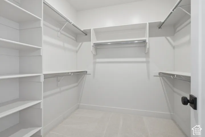 Walk-in closet featuring white built-in shelving, tiered hanging rods, carpeted flooring, and a matte black door knob