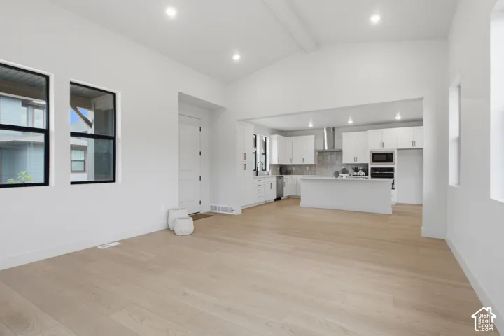 Vaulted ceilings, LVP flooring, recessed lighting, and kitchen featuring white cabinetry with a center island and stainless steel appliances