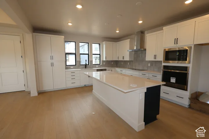 Kitchen featuring white shaker-style cabinetry, quartz countertops, a central island, stainless steel built-in oven and microwave, and LVP flooring