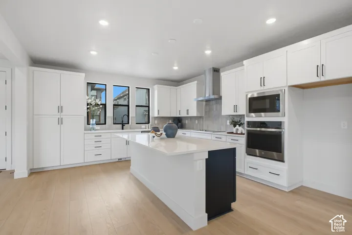 Kitchen featuring white cabinetry, a center island with contrasting base, quartz countertops, LVP flooring, and stainless steel built-in appliances