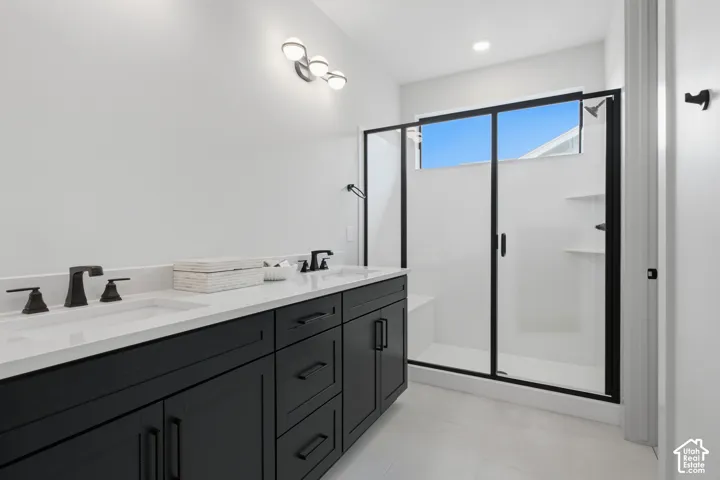 Dual-sink vanity with dark cabinetry, quartz countertop, matte black fixtures, and walk-in shower featuring a glass enclosure with black framing