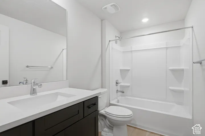 Bathroom featuring a dark-finish vanity with a white countertop and integrated sink, full-width mirror, and a tub-shower combination with built-in shelving