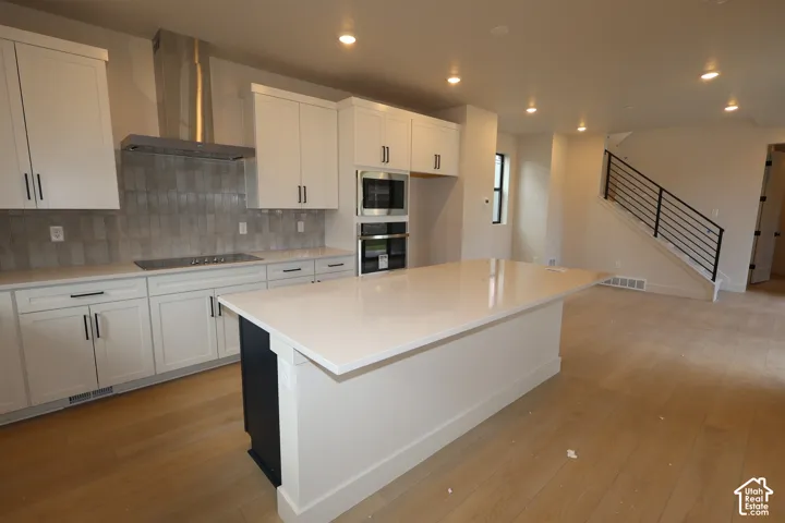 Kitchen featuring white shaker cabinetry, an expansive center island with a stone-finish countertop, stainless steel appliances, a tile backsplash, and LVP flooring