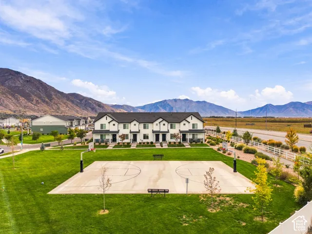 Exterior view of a multi-unit residential building featuring a concrete basketball court, expansive manicured lawn, and mountainous horizon