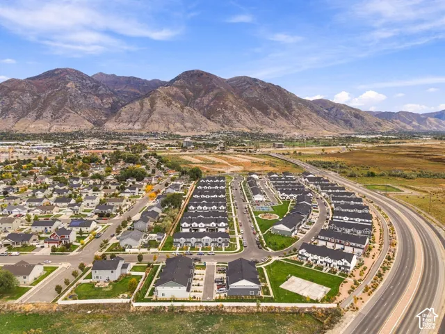 Aerial perspective showcasing a residential community with multi-unit dwellings, manicured lawns, paved street infrastructure, and a prominent mountain range backdrop