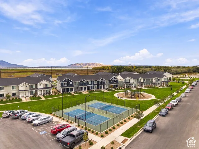 Aerial perspective of community featuring pickleball courts, playground equipment, manicured lawn areas, and mountain backdrop