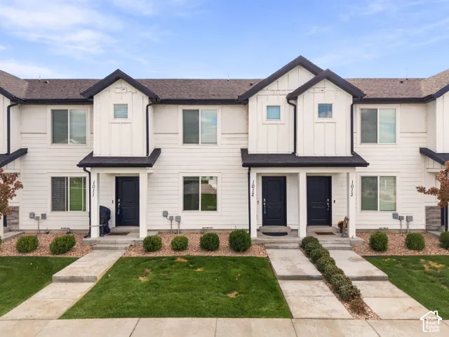 Two-story townhome exterior featuring white vertical and horizontal siding, dark gabled rooflines, stone veneer accents, and individual concrete entry walkways
