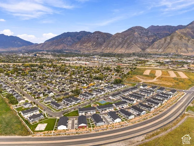 Aerial perspective featuring multi-level residential structures, landscaped green space, a dedicated sports court, and a mountain range backdrop